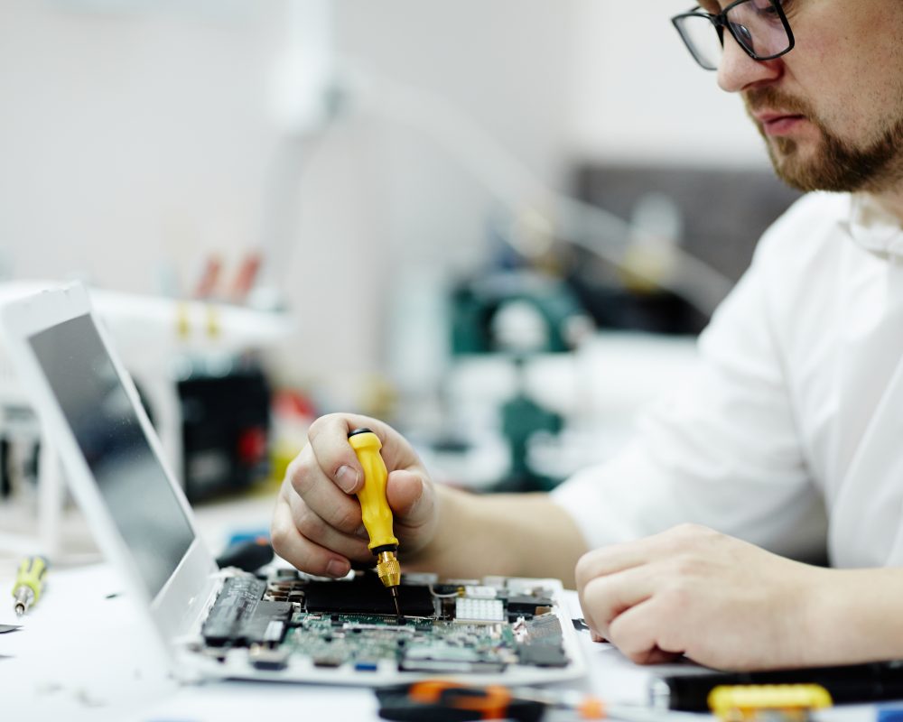 Portrait of modern working on assembling circuit board using screwdriver and tools on table in maintenance shop